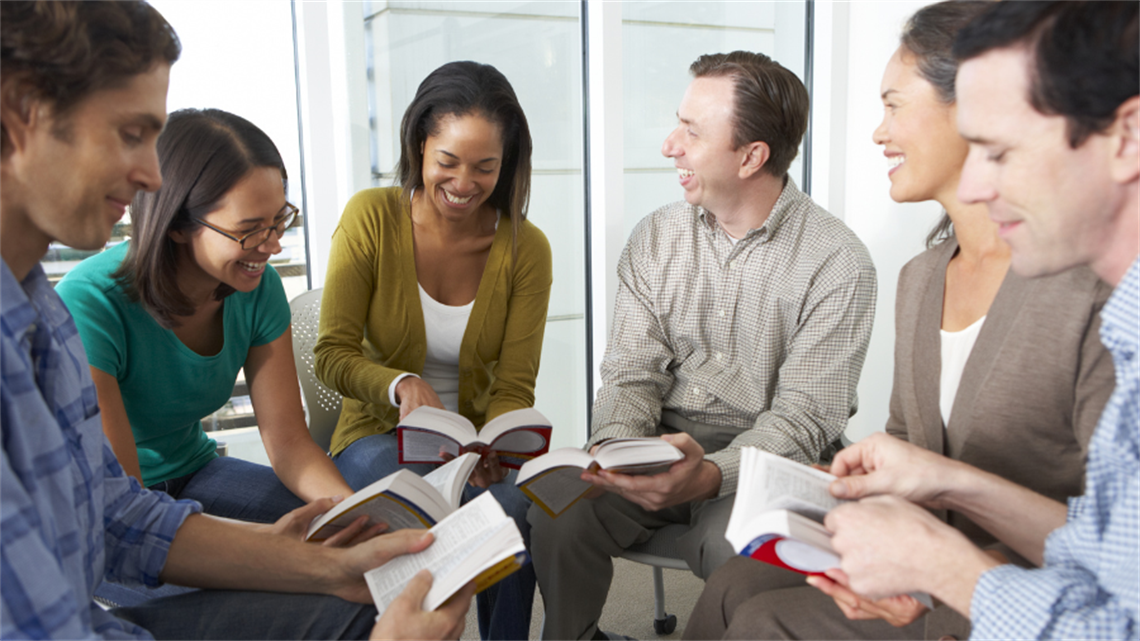 Group of people sitting in circle reading books smiling