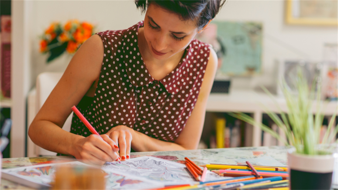 Woman sitting at desk looking down while colouring in book
