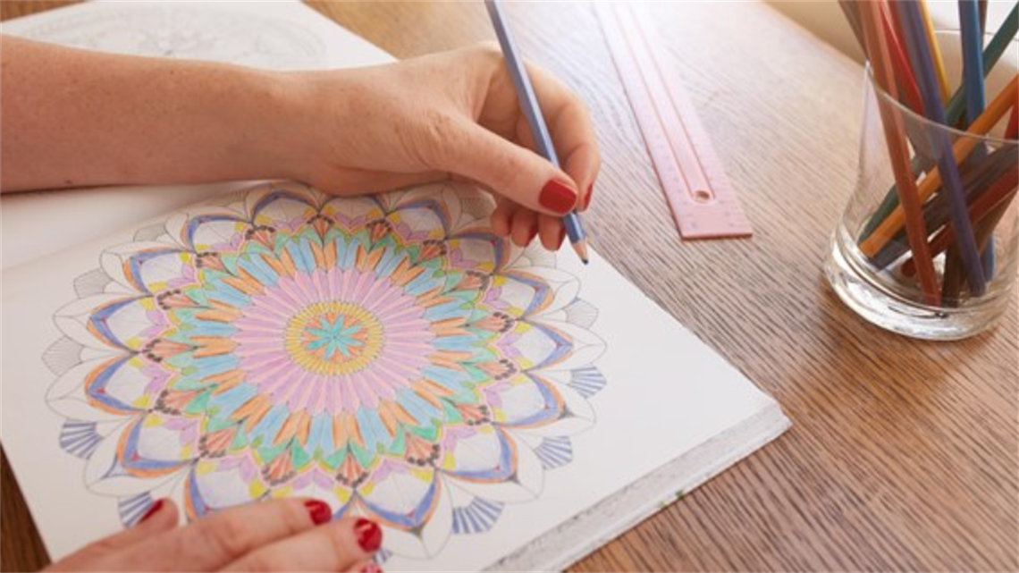 Hand holding pencil colouring in image in book Hand holding pencil colouring in image in book