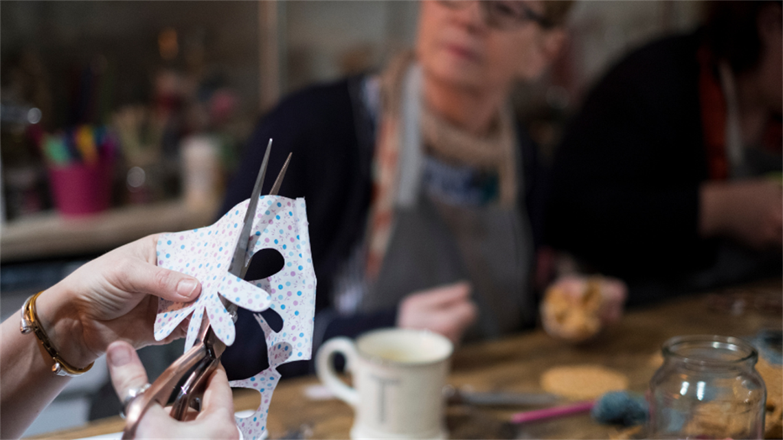 Close up of paper being cut with mug on table and person in background Close up of paper being cut with mug on table and person in background