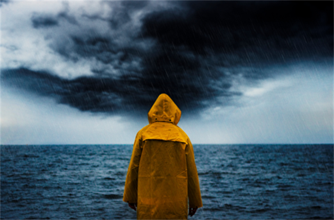 Back of person in yellow raincoat facing storm clouds over the ocean with rain coming down