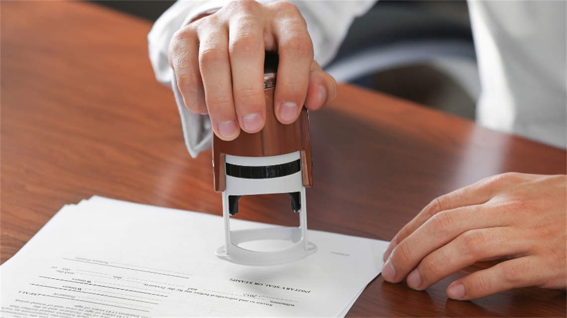 Close up of hands holding stamp notarising paperwork
