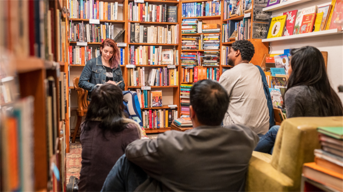 Group of adults sitting surrounded by books listening to a story