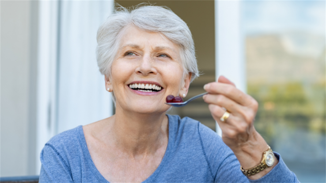 A woman smiling with a spoon of fruit